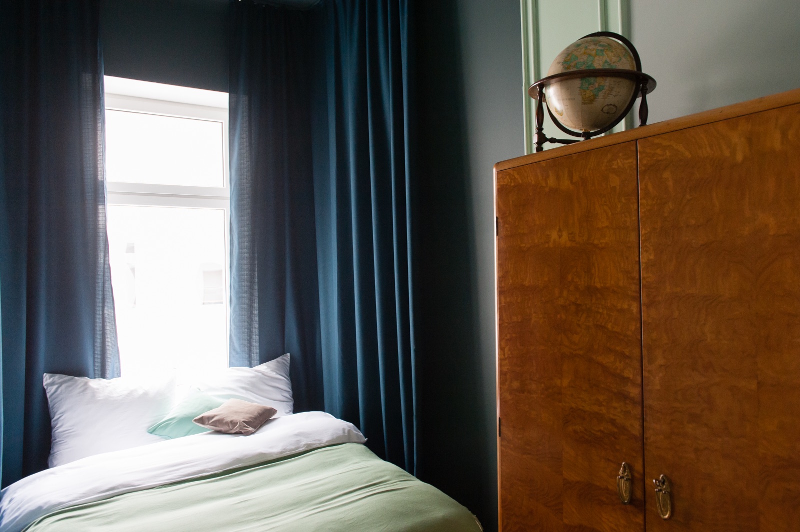 Appartement meublé à Vienne, chambre bleue avec armoire en loupe de bois, globe et lit vert sauge