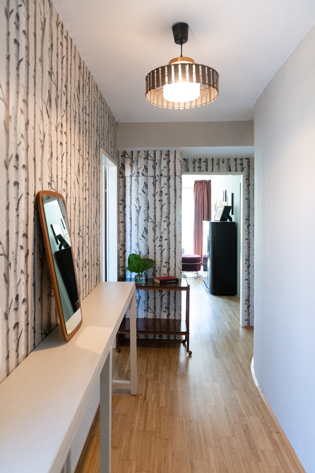 Furnished apartment in Vienna, bedroom with pendant light and brass side table, hallway with birch wallpaper and living room with grey velvet sofa