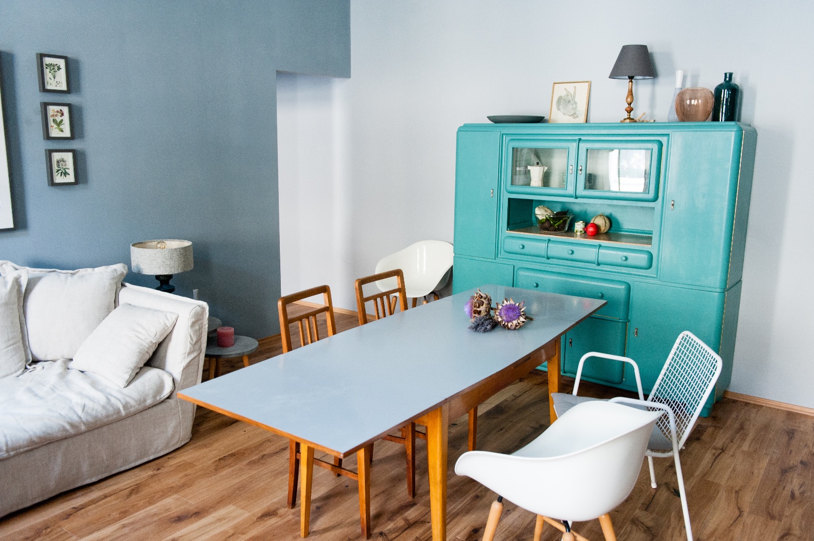 Wohnzimmer mit hellgrauem Esstisch auf Eichenbeinen, türkisem Vintage-Schrank und hellem Sofa, dazu zwei Schlafräume für eine Familie auf Zeit in Wien