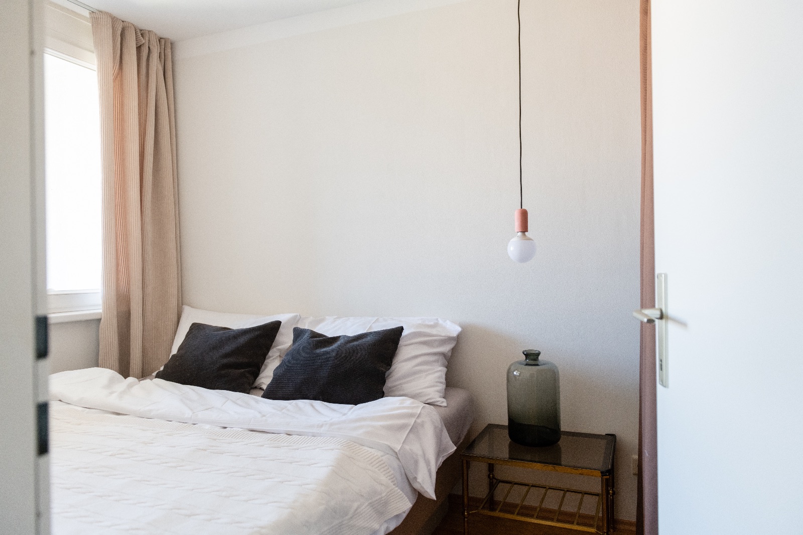 Möbliertes Apartment in Wien, Schlafraum mit Pendelleuchte und Messingbeistelltisch, Flur mit Birkentapete und Wohnzimmer mit grauem Samtsofa